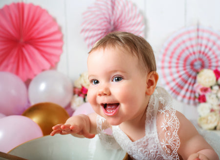 Smiling baby girl enjoying a birthday cake smash photoshoot